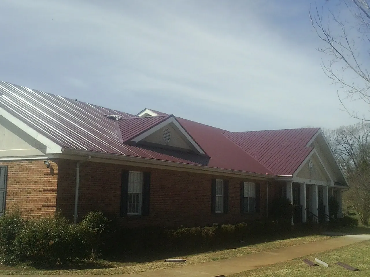 Red metal roof with gabled entries on a long brick building, from a Hail Damage Roof Repair job in Denham Springs