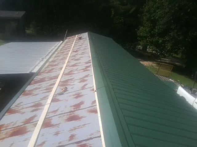 Old rusted panels beside newly installed green metal roofing — Wind Damage Roof Repair by Roofing Brothers in Denham Springs
