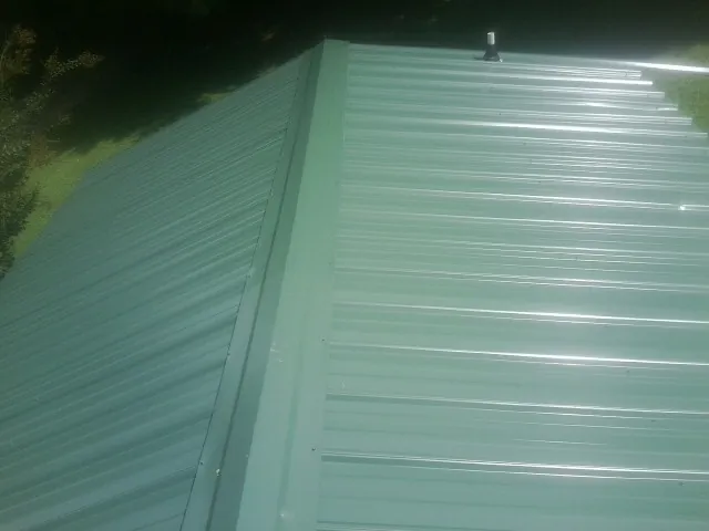 New green metal panels meeting at the ridge of a roof — Flat Roof Repair work by our crew in Denham Springs
