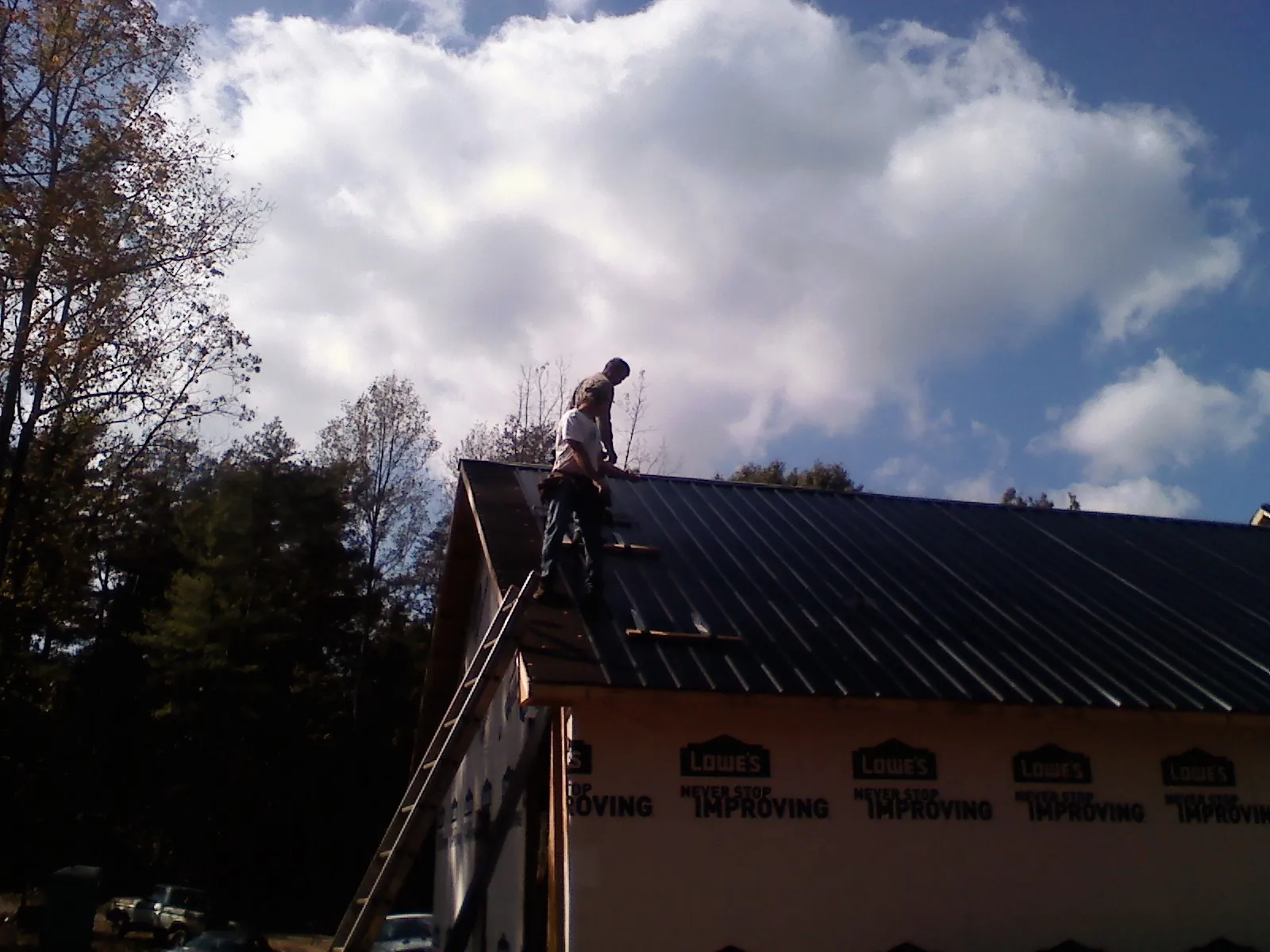 Roofer fastening dark metal panels high against a cloudy sky, from a Roof Inspection job in Denham Springs