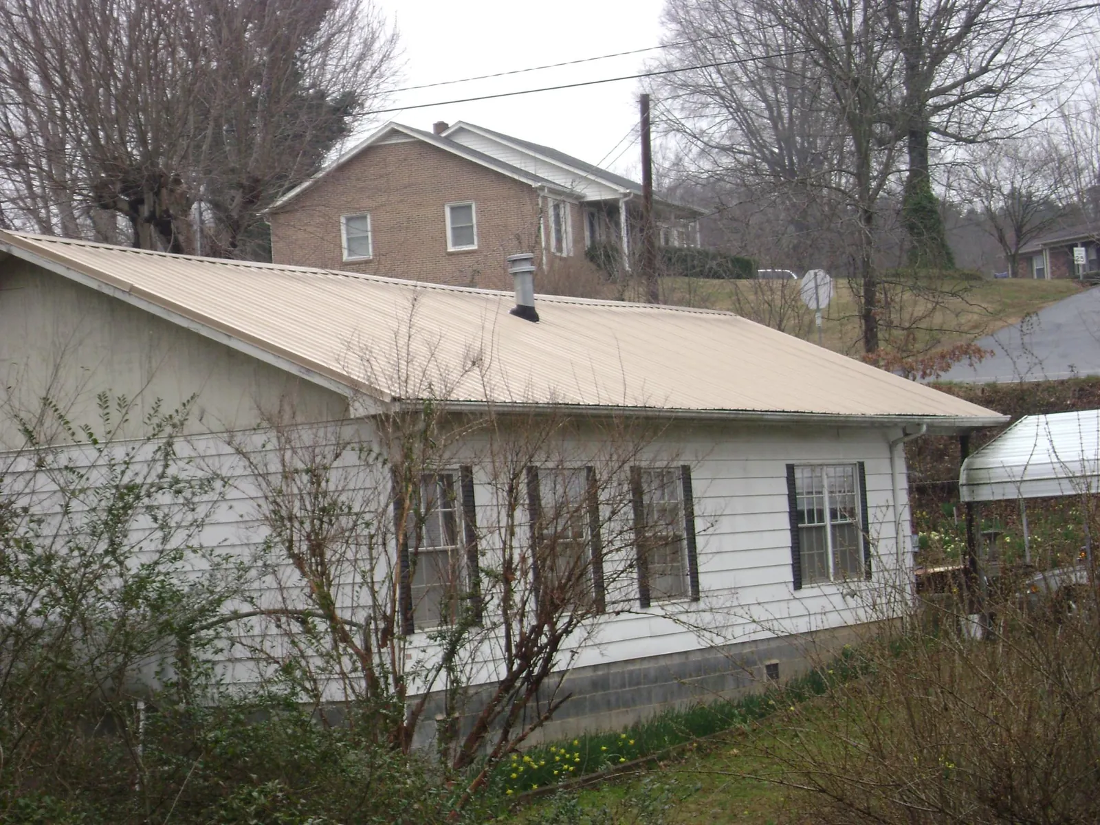 Tan metal roof on a white sided house set into a hillside — Commercial Roofing by Roofing Brothers in Denham Springs