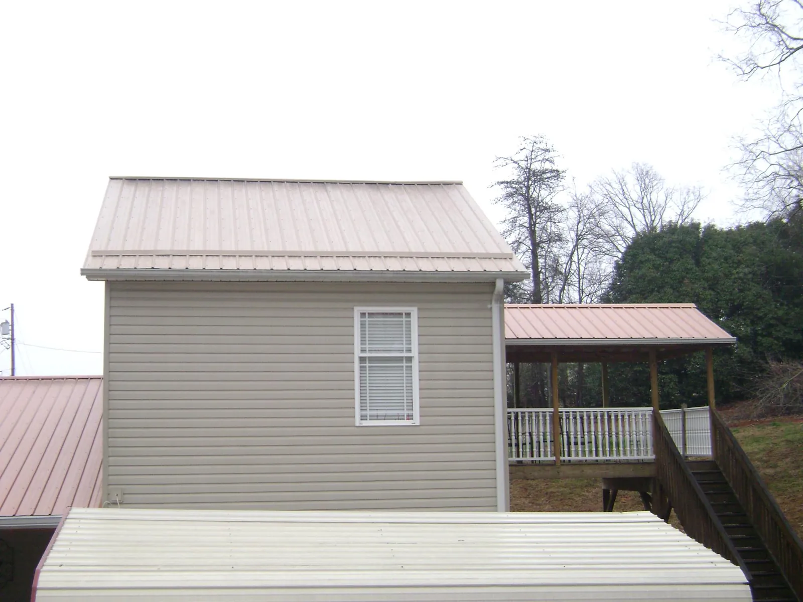 Tan metal roofs on a two story addition and attached porch, from a Roof Replacement job in Denham Springs